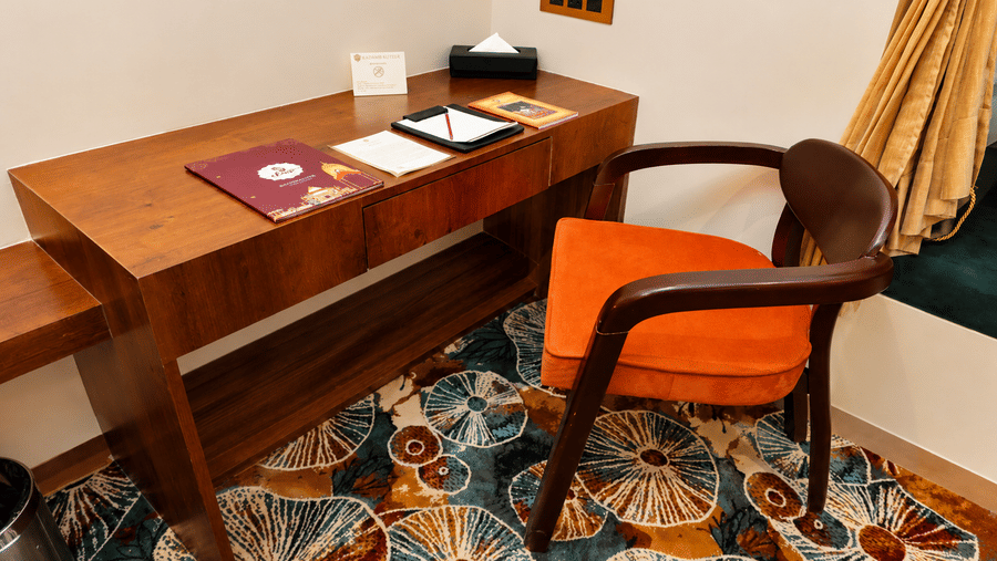 Guest room with a wooden writing desk, chair, and vibrant patterned carpet at Kadamb Kuteer, Vrindavan.