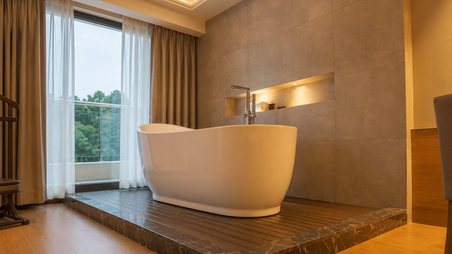 Freestanding bathtub on a raised platform by a window in the Royal Club Room at Kiranshree Grand Hotel.