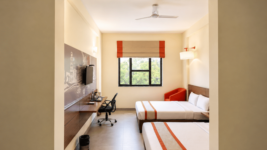 Max Family Room at Max Hotel Jabalpur with twin beds, a wall mounted TV, work desk and large window.