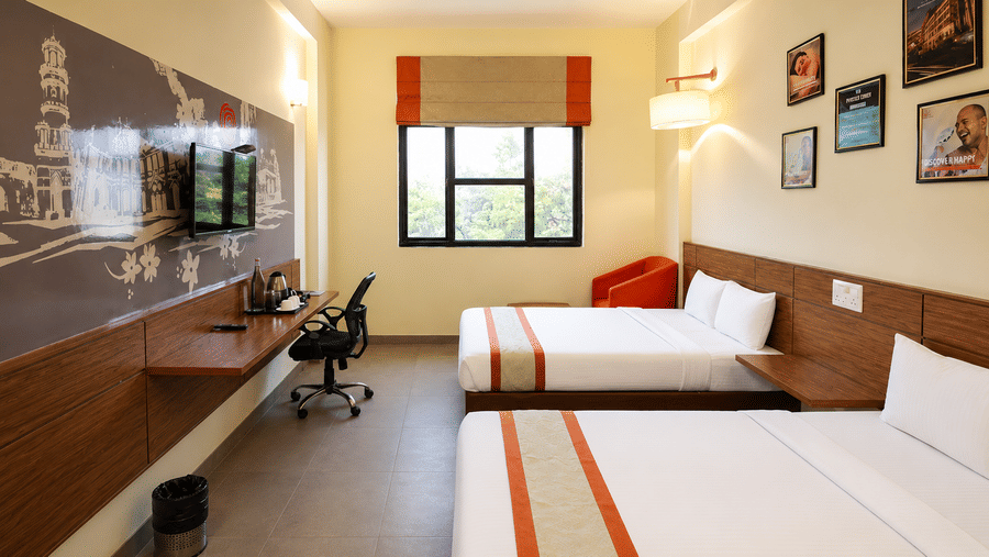 Max Family Room at Max Hotel Jabalpur with twin beds, a work desk, wall mounted TV and large window.