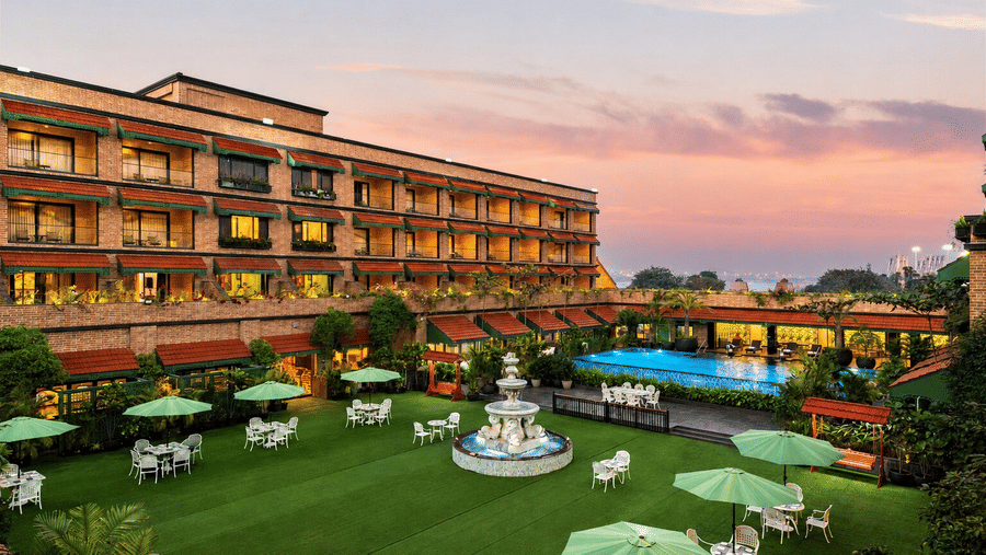 A wide green lawn with a central water fountain and sun umbrellas set against a sunset sky at MAYFAIR Bay Resort, Paradeep.