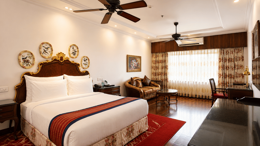 King Suite at MAYFAIR Himalayan Spa Resort Kalimping featuring a king size bed, a ceiling fan, a cabinet table, a sofa with centre table, and AC, and a work desk with chair.