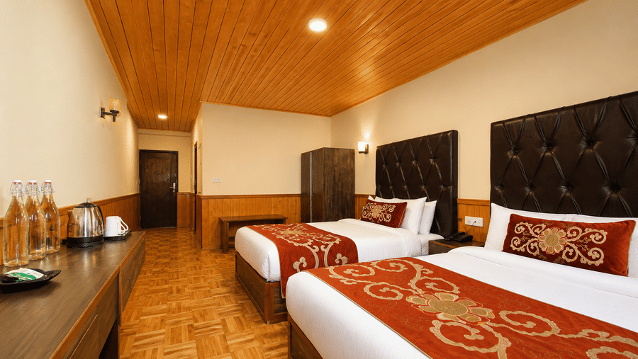 Beds with pillows fill the Family Room at Orsino Khangri Karpo Retreat & Spa, Lachung. A cabinet with bottles sits on the left side. A door leads out from the back of the space.