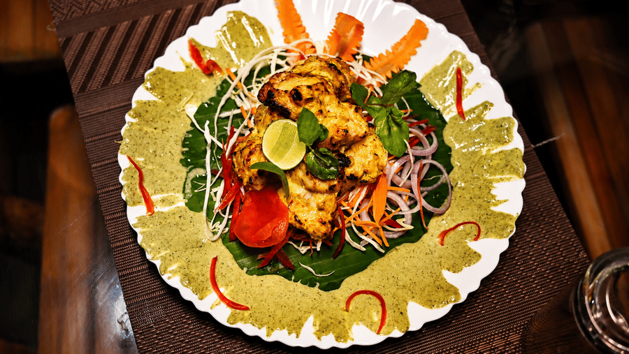 Overhead view of a plated dish with rice, curry and grilled prawns, garnished with lime, chilli and fresh coriander on a white ceramic plate.