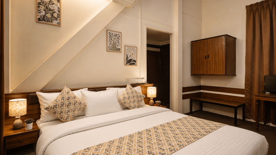 Dressed double bed with patterned throw pillows, bedside lamp, and slanted beam architecture in a Wind Chalet room.