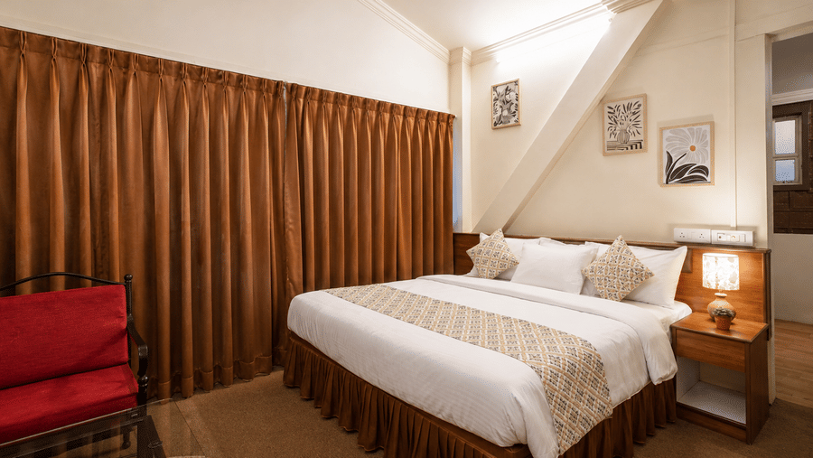 King double bed with white linen, bedside lamp, red armchair, and long brown drapes inside a Wind Chalet bedroom.