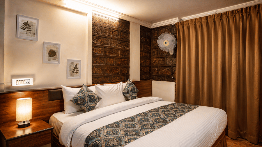 Cosy double bed at Wind Chalet with patterned runner, decorative cushions, bedside lamp, and warm wall lighting.