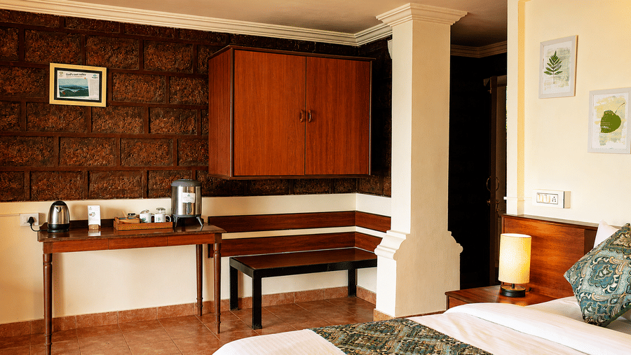 Tea maker table, wooden wall cabinet, and bench seat in a Wind Chalet bedroom near a bed with green cushions.