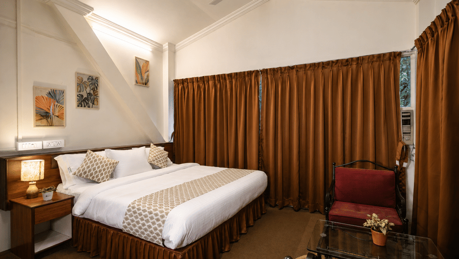 Double bed with patterned runner, bedside table, lamp, and drawn brown curtains in a Wind Chalet guest suite.