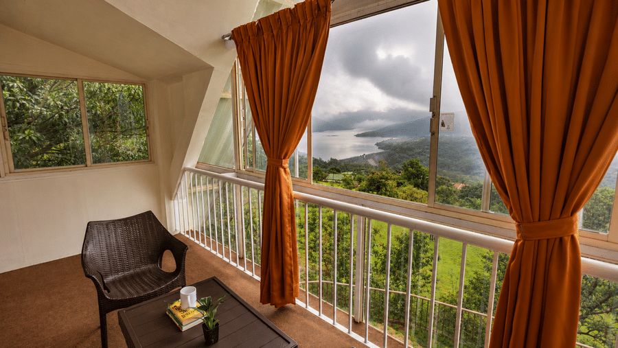 Covered balcony at Wind Chalet with seating table, armchair, and large glass windows viewing hills and cloudy sky.