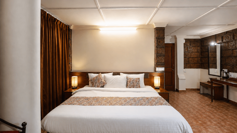 Front view of a double bed with white linen, brown runner, and lit bedside lamps in a Wind Chalet guest room.