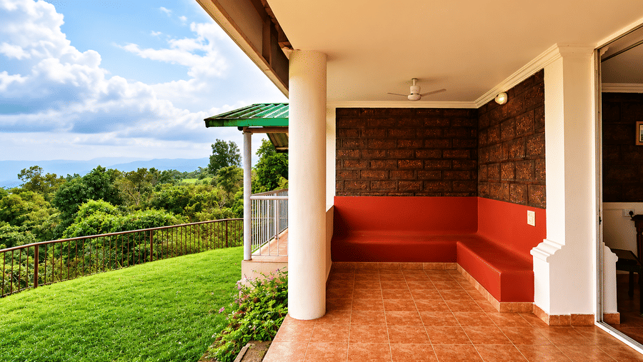 Covered outdoor veranda at Wind Chalet with red built-in bench, tiled floor, and views of lush lawn and blue sky.