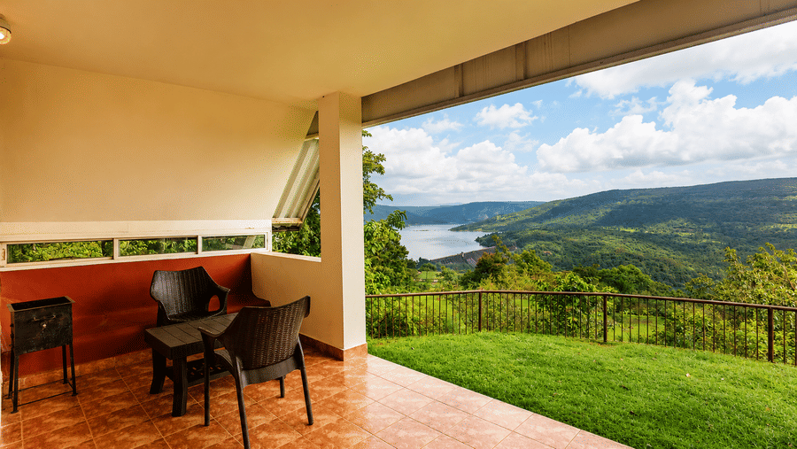 Covered patio terrace at Wind Chalet with seating overlooking a grassy lawn, rolling hills, and a distant lake.