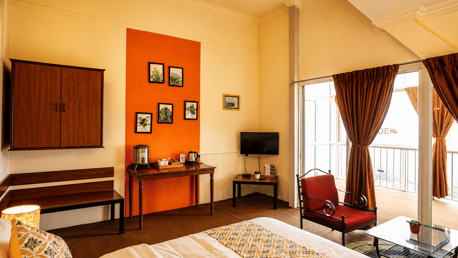Angle view of a Wind Chalet guest suite showing a made double bed, orange accent wall, red armchair, and desk area.