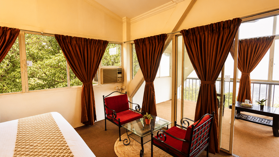 Cosy seating corner in a Wind Chalet bedroom with red armchairs, coffee table, and large window overlooking greenery.