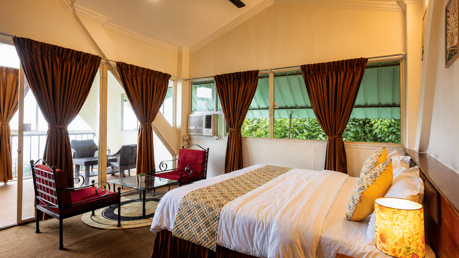 Spacious guest bedroom at Wind Chalet with king double bed, yellow accent cushions, bedside lamp, and red chairs.