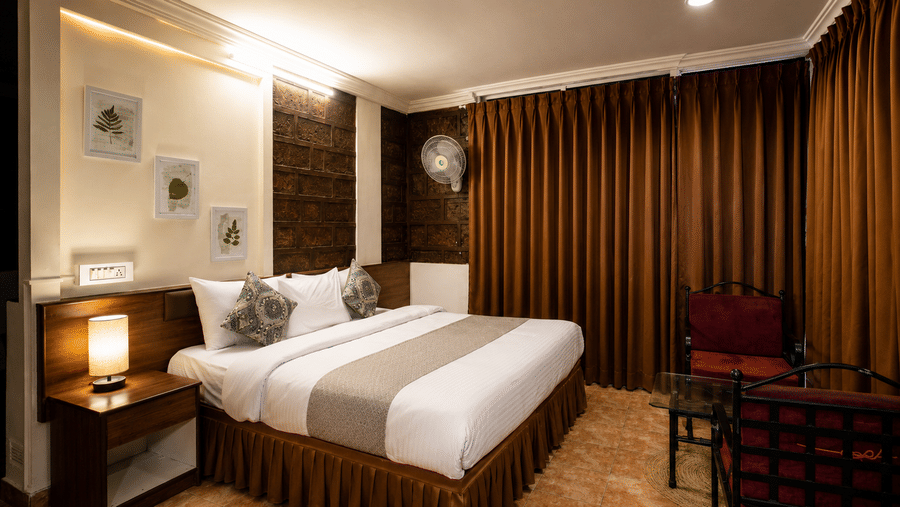 Bedroom at Wind Chalet featuring a double bed with grey runner, bedside lamp, wall art, and long brown curtains.