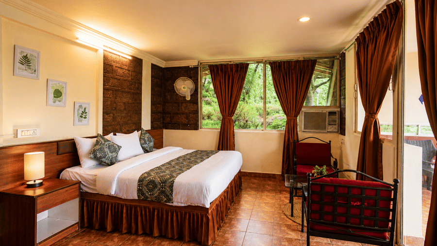 Wind Chalet bedroom with tiled flooring, double bed, bedside table, lamp, brown drapes, and red seating furniture.