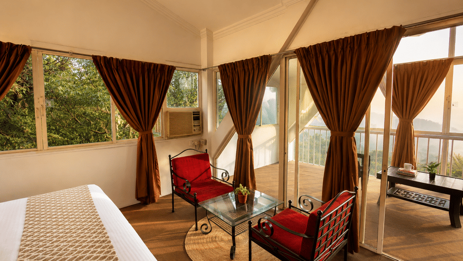 Elevated view of a Wind Chalet guest suite featuring a made bed, red armchair lounge, and floor-to-ceiling windows.