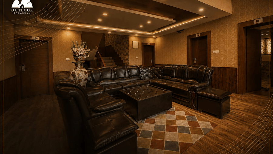 A lounge area at Hotel Outlook, Pahalgam, with a large sectional sofa, a coffee table, patterned rugs, and warm lighting on the ceiling.