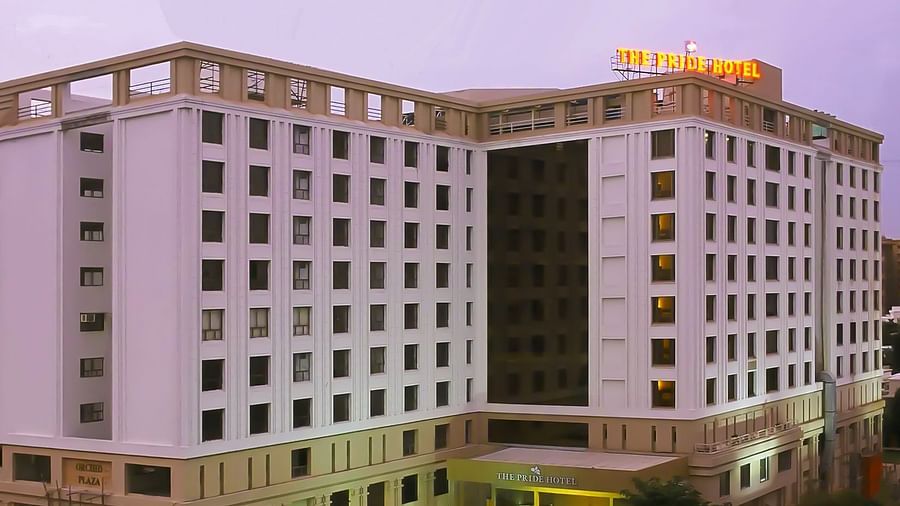 Facade of Pride Plaza Ahmedabad hotel with its name lit up atop the building, set against a glowing sunset sky for a striking evening view