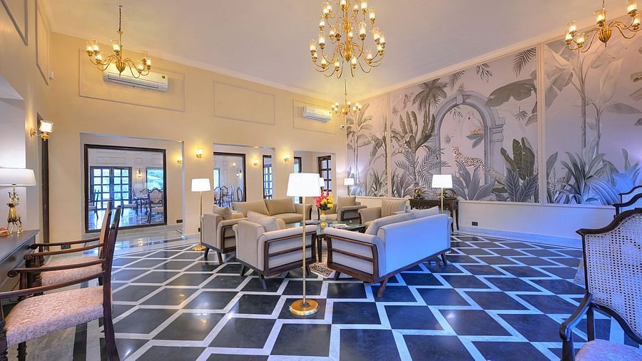 Spacious hotel lounge with elegant chandeliers, patterned black-and-white flooring, beige seating, and a wall mural featuring jungle-themed artwork with tropical leaves and a leopard - Singhvilas, Ranthambore