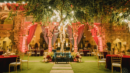 A courtyard at Tijara Fort-Palace - 19th Century, Alwar, with a central tree, decorated arches, seating, and tables set for an event.