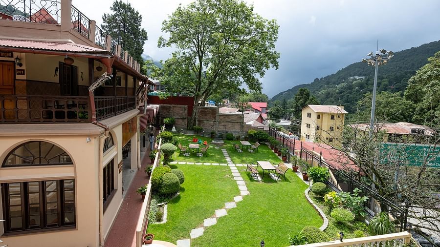 Aerial view of The Pavilion, Nainital's landscaped gardens with geometric lawn patterns, pathways, and traditional buildings nestled in forested hillside.
