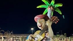 The night view of the a boy big statue playing guitar surrounded by big palm tree and lights