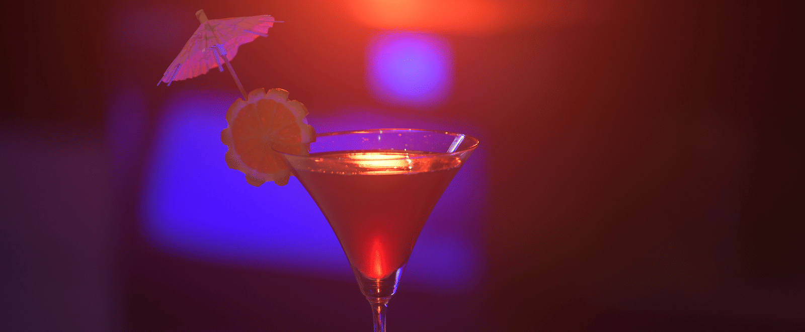 A bright cocktail garnished with fruit, glowing under neon lighting at Hotel Sonar Bangla Mayapur.