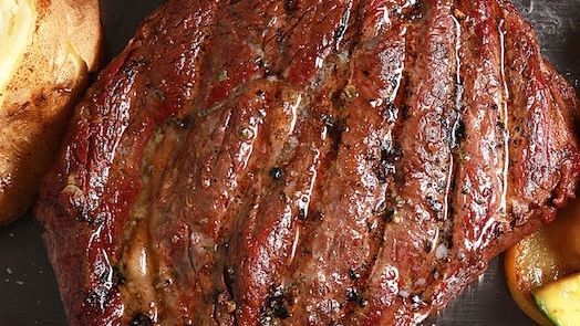 A close-up shot of a large, grilled steak with visible grill marks and a rich brown color