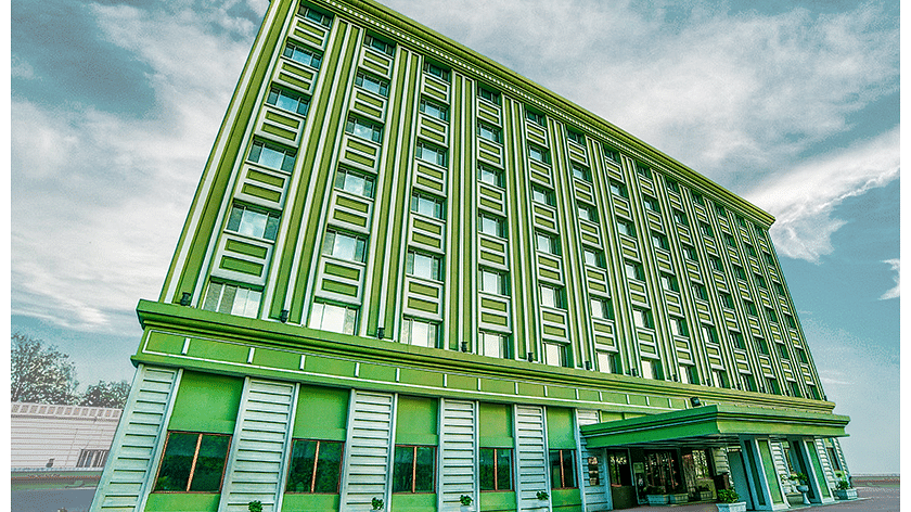 Exterior view of the tall green Tara building with multiple windows and a slanted architectural design under a cloudy sky.
