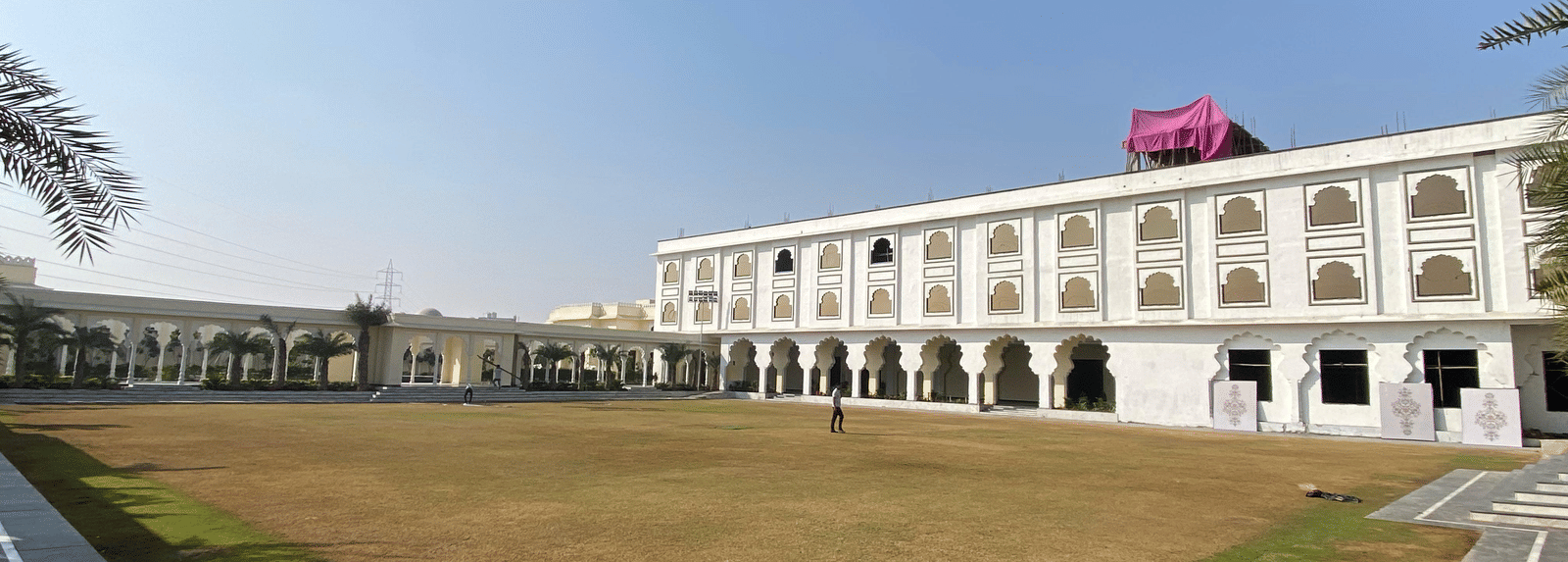 Large open lawn area bordered by multi-storey white building with arches at Beelwa Palace, Jaipur