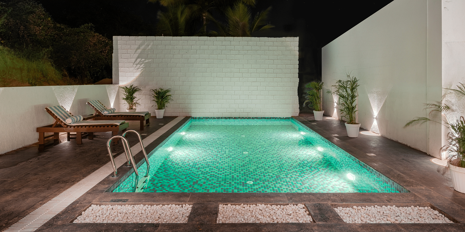 Outdoor pool area with green lighting and privacy walls at night at Bedzzz Xclusiv Morjim, Goa