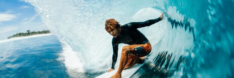 A man surfing on a wite surf boat with a giant wave falling over his head.