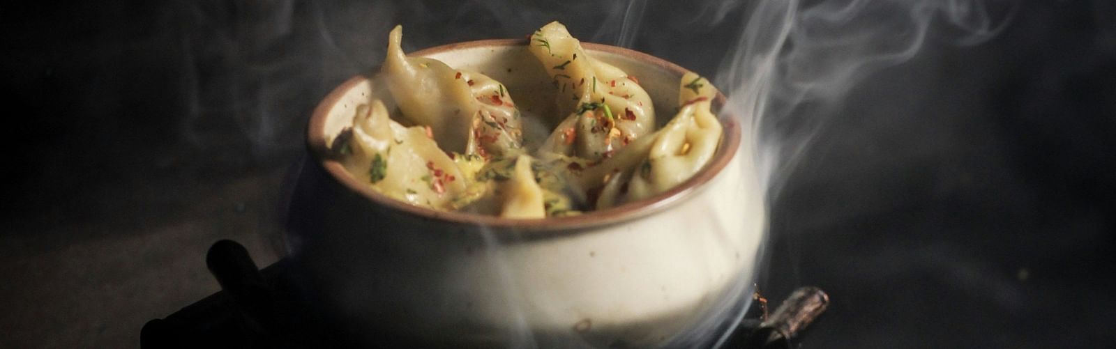 A plate of steaming hot momos with visible wisps of steam rising away.