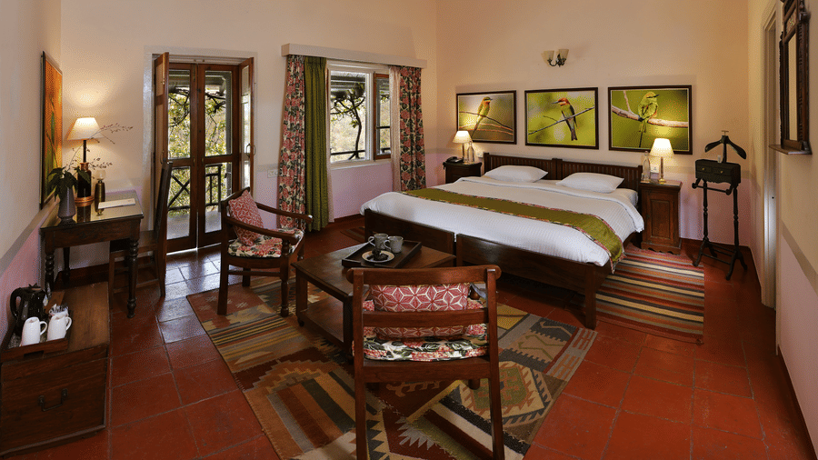Premium bedroom with wooden bed seating area side tables and soft lighting offering comfort and space at Neemrana’s Glasshouse on The Ganges designed for extended and relaxing stays