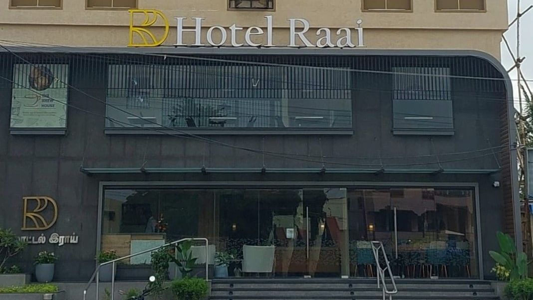 Facade of Hotel Raai, Hosur featuring four storey building. The ground floor has glass walls at the entrance and the other floors have concrete walls with long windows facing the street.