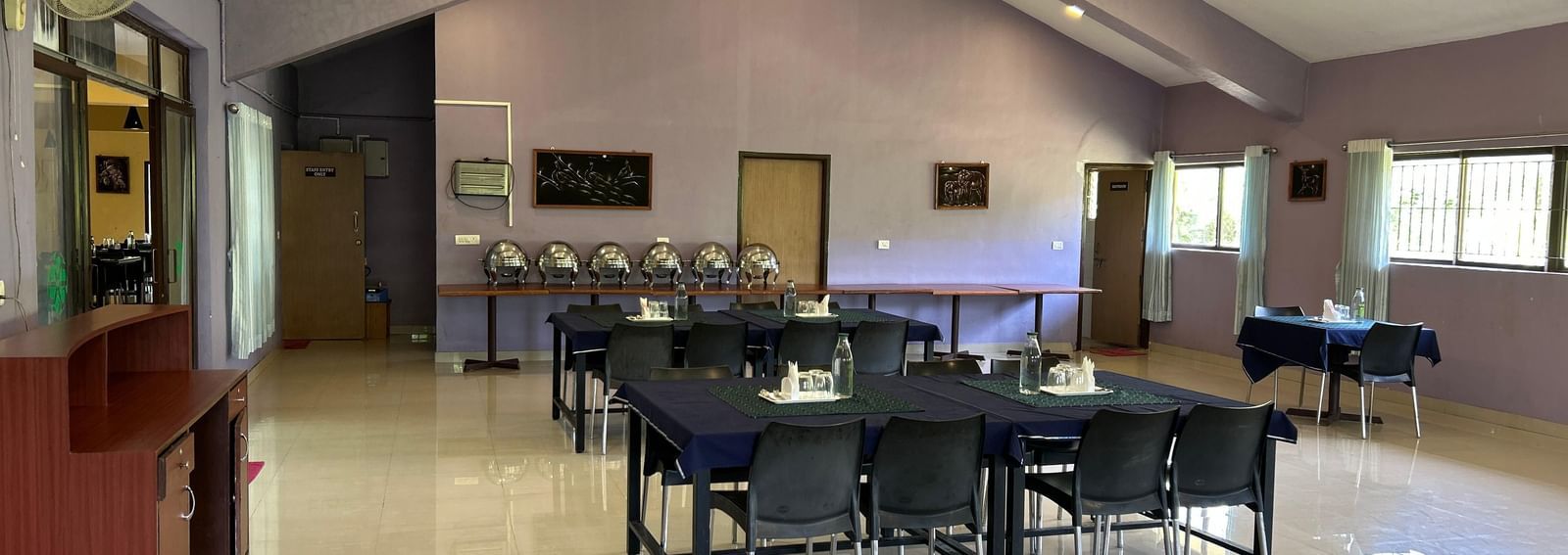 Indoor dining setup with tables, chairs, light purple walls, and ceiling lights at Paradise Wild Hills Resort, Kollur.