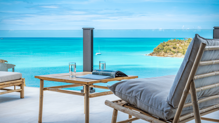 A balcony with a view of the ocean, with lounge chairs and a table at Tamarind Hills Resort and Villas, Antigua.