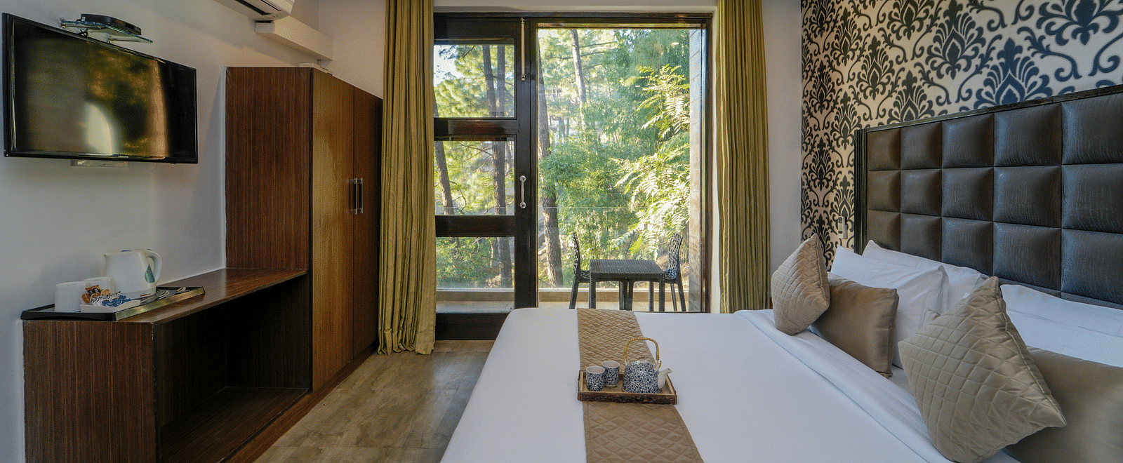 The deluxe room with a bed, a flat screen TV, an air-conditioner, and the glass door leading to the balcony with forest view - DLS Whispering Winds