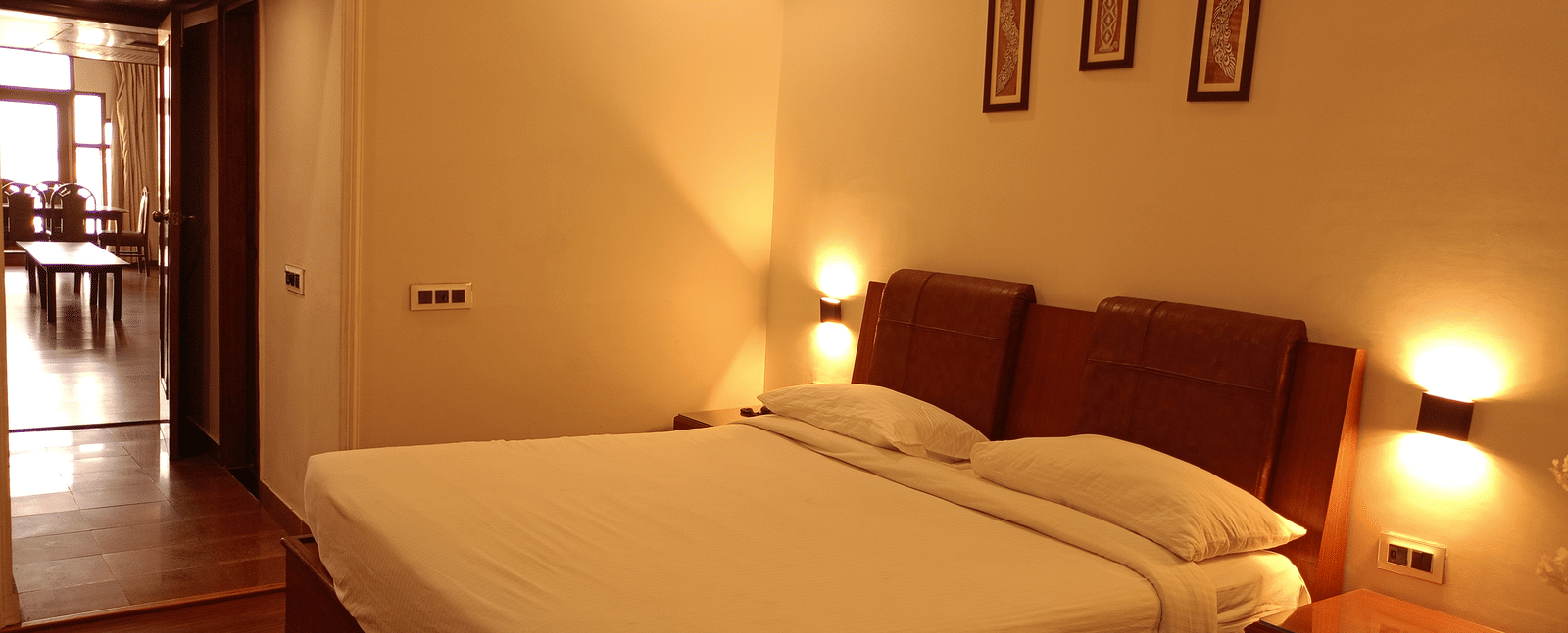 Guest room at Hotel Gold, Panipat featuring a bed, side tables, and framed wall art.