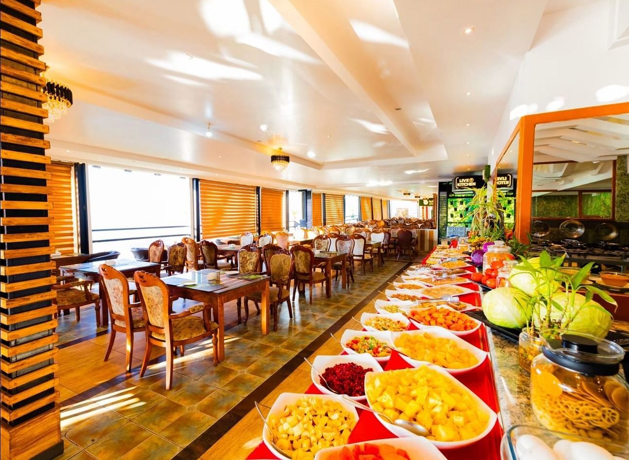 An image of a dining area where there's a buffet served at one side and a seating arrangements made with chairs and tables on another side - Parakkat hotel & resorts