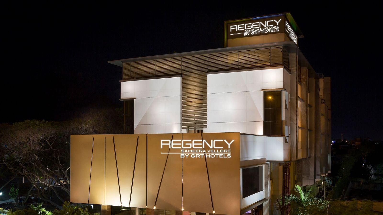  Modern multi-story hotel building with warm lighting, a prominent hotel sign, and landscaped grounds