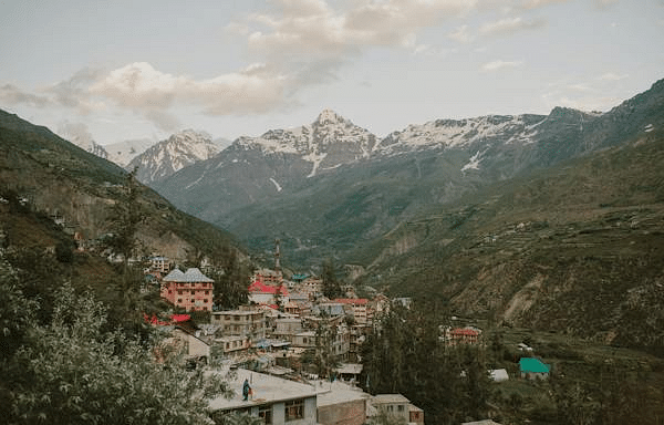 A picturesque village at the foot of the Himalayas is nestled in a lush valley, surrounded by towering peaks and vibrant greenery. The charming homes and pathways reflect the simplicity of village life, offering a serene escape into nature’s beauty.