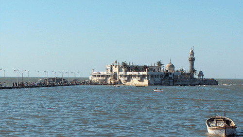 An overview of the Haji Ali Dargah in Mumbai as seen from afar with a boat in the foreground.