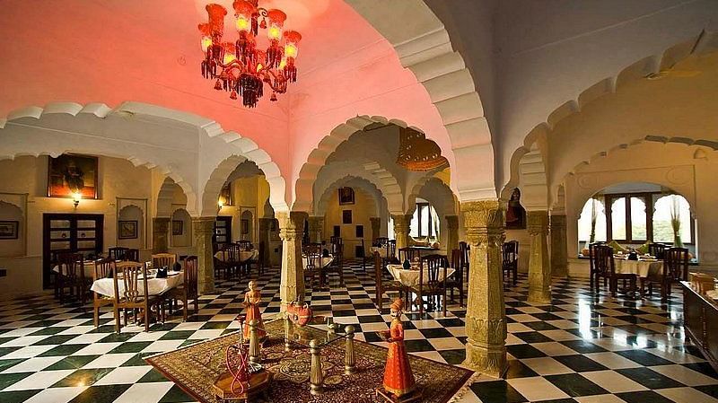An elegant dining hall at Fort Barli, with arched ceilings, checkered floors, and a vibrant chandelier, blends historical architecture with a refined dining experience.