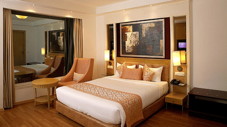 A spacious double room at Eastlynn Collections HUDA City Centre, Gurugram featuring a large bed, seating area, warm lighting, and modern decor.