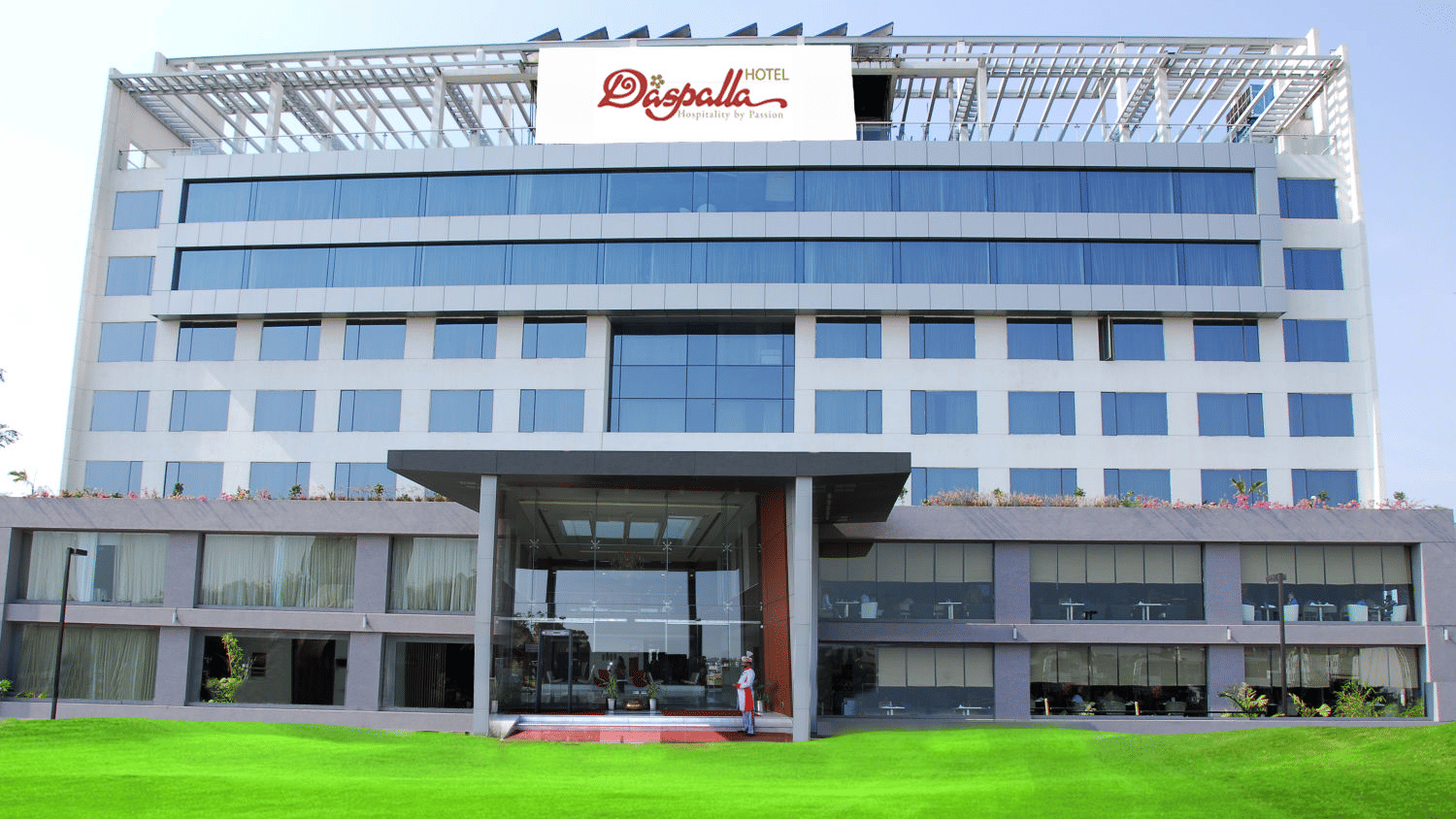Daspalla Hotel exterior with glass facade white building green lawn and welcoming entrance staff standing at the front door
