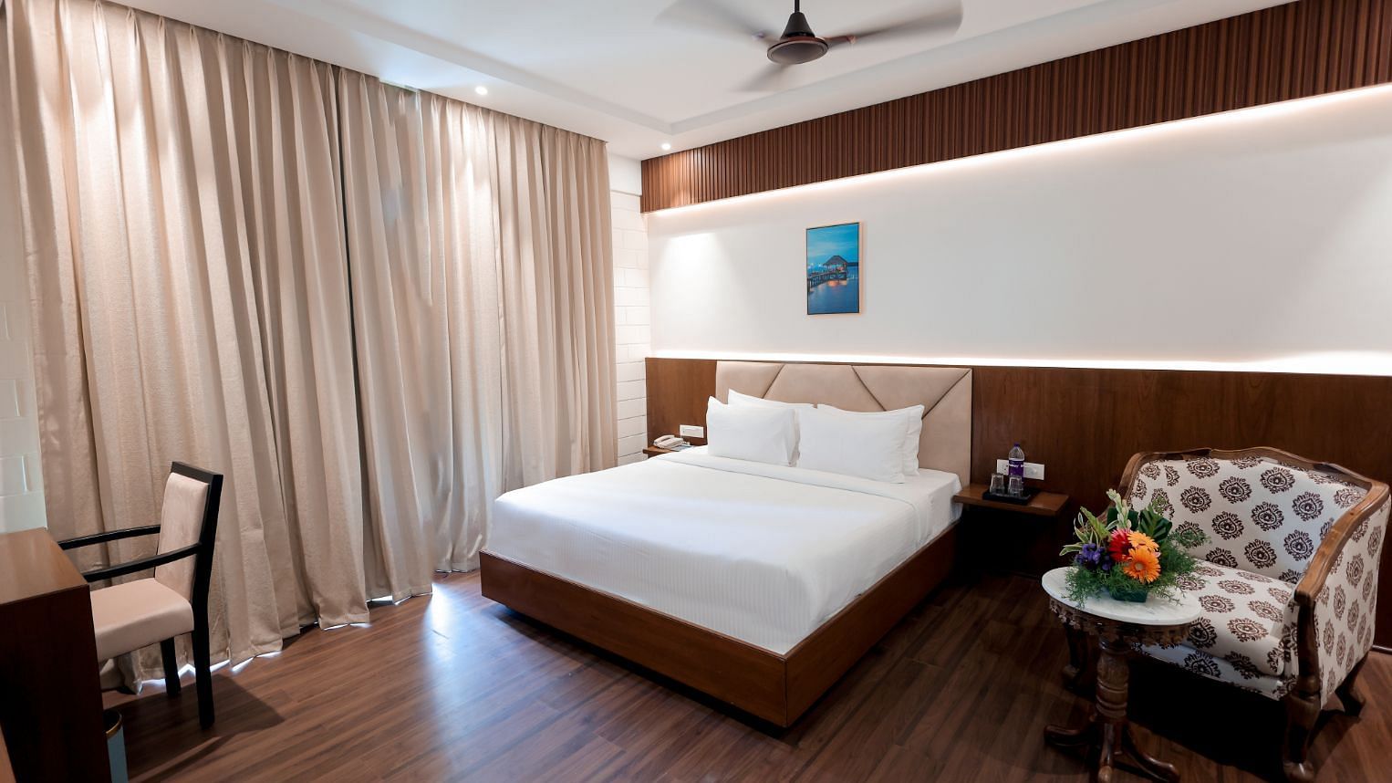 A bedroom with double bed, chair, round table and framed art work at Trishvam Symphony, Krishnagiri